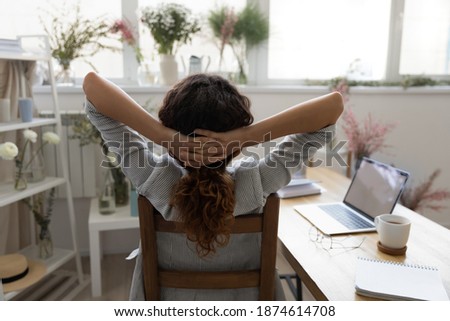 When all is done. Back rear view of happy young female florist sitting on chair in cozy studio pleased with work results. Creative interior designer stretching with hands behind head resting relaxing