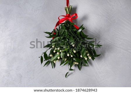Mistletoe bunch with red bow hanging on grey wall. Traditional Christmas decor