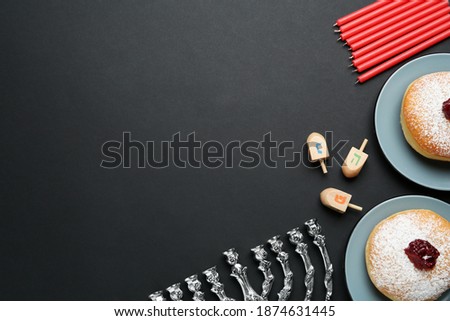 Hanukkah traditional menorah, candles, doughnuts, dreidels with letters He, Pe, Nun, Gimel on black background, flat lay. Space for text