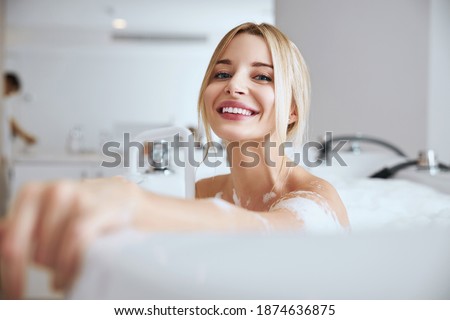 Close up portrait of elegant Caucasian woman enjoying water procedure while looking and posing at the photo camera in room indoors