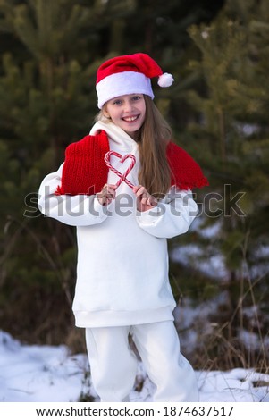 Child playing in snow on Christmas vacation. Winter outdoor fun. Kids play in snowy park on Xmas eve. Little girl in Santa hat,  with heart shaped lollipops
