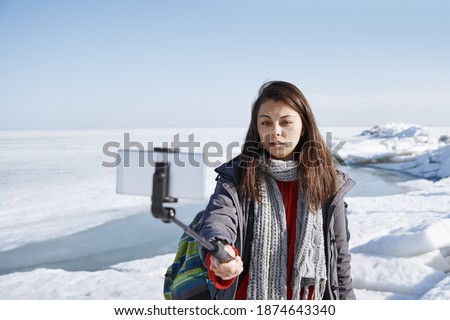Female traveler outdoors at icy landscape using monopod to make selfie picture