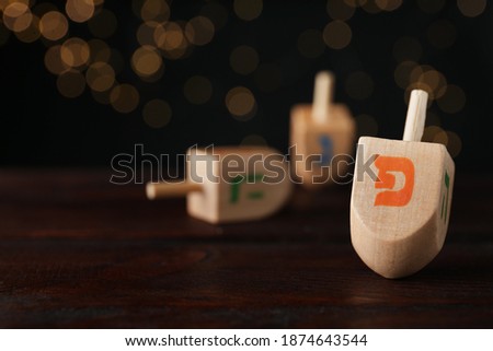 Hanukkah traditional dreidel with letter Pe on wooden table against blurred lights. Space for text