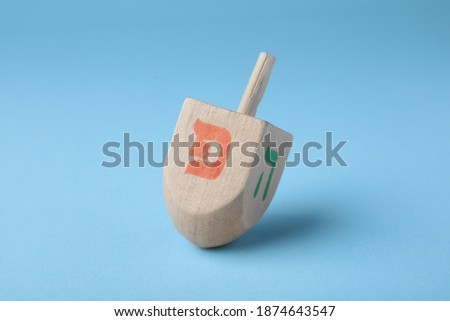 Hanukkah traditional dreidel with letters Pe and He on light blue background