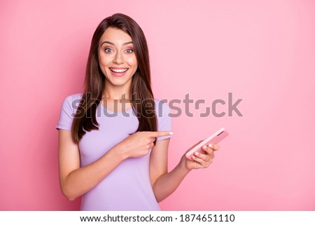 Photo of amazed young girl brown hair hold telephone show pointing gesture dressed casual outfit isolated on pink color background