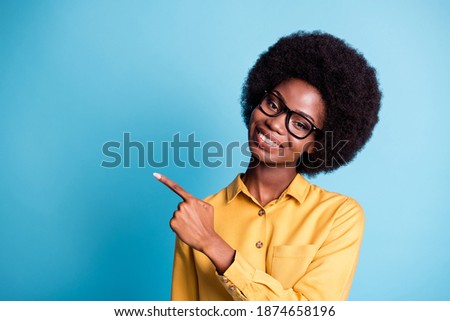 Photo of black skin extensive hairdo girl shiny smile directing finger empty space offer marriage luxury jewelry discounts wear specs yellow shirt isolated blue color background