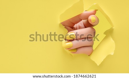 Female hand with yellow nail design. Glitter yellow nail polish manicure. Woman hand on yellow paper background. Royalty-Free Stock Photo #1874662621