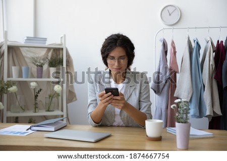 Negotiations online. Interested young woman florist designer using cellphone at workplace in home office studio. Tailor dressmaker calling contacting client customer supplier to discuss order details