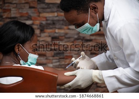 african doctor injecting an african woman with a vaccine for covid 19 Royalty-Free Stock Photo #1874668861