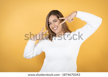 Young caucasian woman over isolated yellow background Doing peace symbol with fingers over face, smiling cheerful showing victory