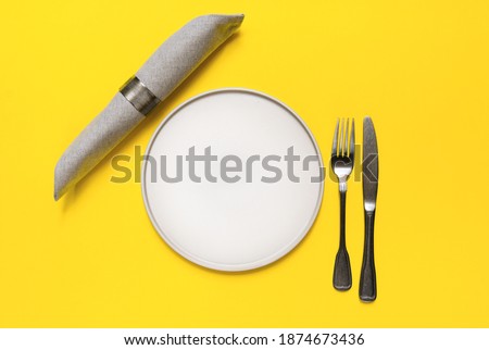 Table setting in the trendy colors - Yellow and Gray. grey plates fork knife napkin on yellow background. 