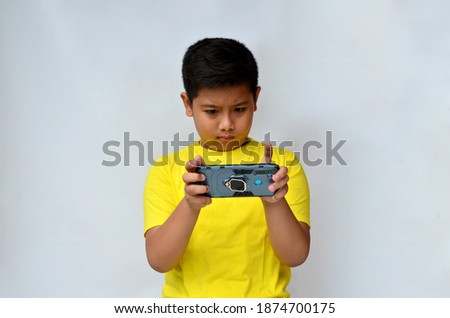 portrait of an Asian boy with an expression playing a game on a smartphone, wearing a yellow shirt on a white background