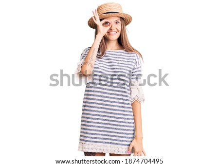 Beautiful caucasian woman wearing summer hat doing ok gesture with hand smiling, eye looking through fingers with happy face. 