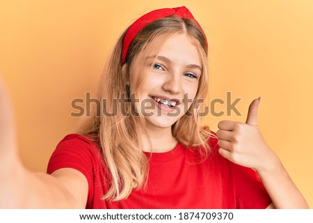 Beautiful young caucasian girl taking a selfie photo smiling happy and positive, thumb up doing excellent and approval sign 