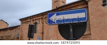 Horizontal banner  blue and white arrow traffic sign in a European city street. One way turn on the left sign.