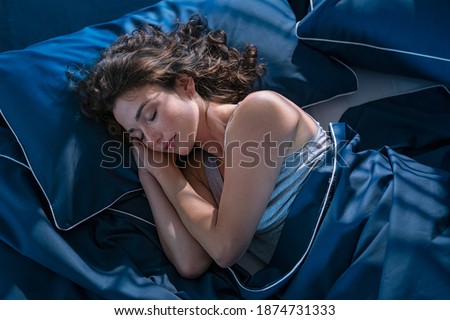 Top view of young beautiful woman dreaming in bed and relaxing at night. High angle view of woman with closed eyes sleeping well at home in the dark. Beautiful girl sleeping peacefully under late. Royalty-Free Stock Photo #1874731333