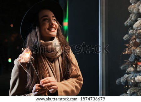 Woman in warm clothes holding burning sparkler outdoors