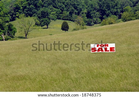 Acreage and farmland in the Tennessee hills are for sale.  Large meadow filled with green grass.  White "for sale" sign has red lettering.
