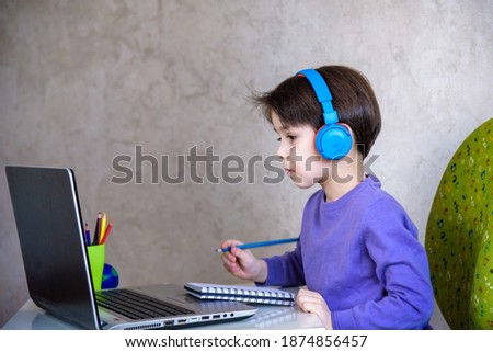 Happy preteen boy sitting on the couch or desk while using a laptop and headphones at home. Online chatting with his school classmates during lockdown.