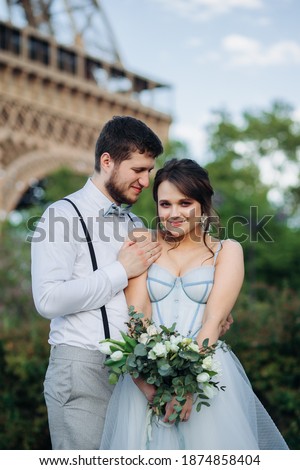 Newlyweds in love on the background of the Eiffel tower. A girl in a blue dress with a wedding bouquet.