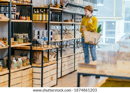 Young Caucasian Woman Buying Superfoods in Zero Waste Shop. Lots of Healthy Food in Glass Bottles on Stand in Grocery Store. No plastic Conscious Minimalism Vegan Lifestyle Concept. Royalty-Free Stock Photo #1874861203