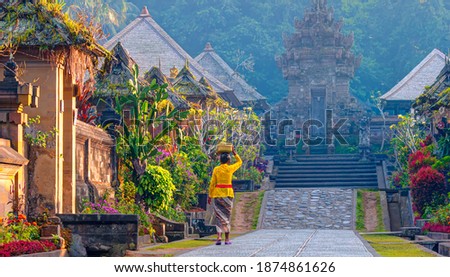 Balinese woman in traditional costume walking on the old street - Penglipuran is a traditional oldest Bali village at Bangli Regency - Bali, Indonesia   Royalty-Free Stock Photo #1874861626