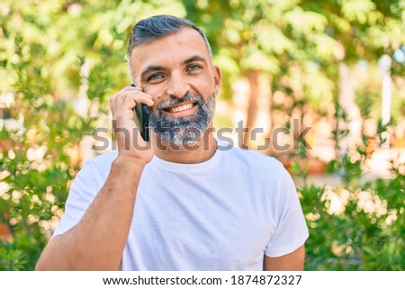 Middle age grey-haired man smiling happy talking on the smartphone at the park