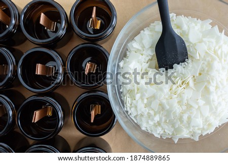 Opaque and amber candles, with wooden wick, ready to make. Soy wax not melted in a glass bowl, with a black spoon. Vegan product without animal cruelty. Royalty-Free Stock Photo #1874889865