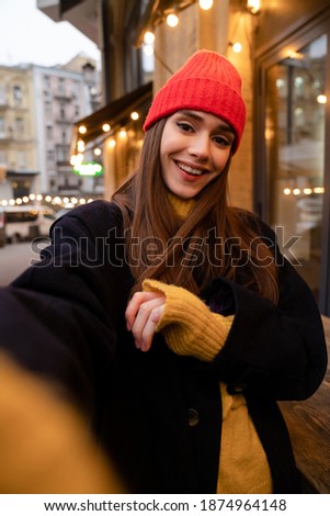 Charming happy girl in hat smiling and taking selfie photo at city street