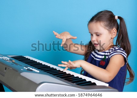 close-up of a happy girl playing a melody on the keys of an electronic synthesizer, studying in an online music class, isolated on a blue background.