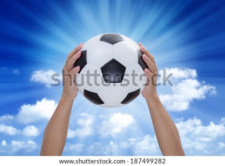 Soccer ball in hands with blue sky and lightray background