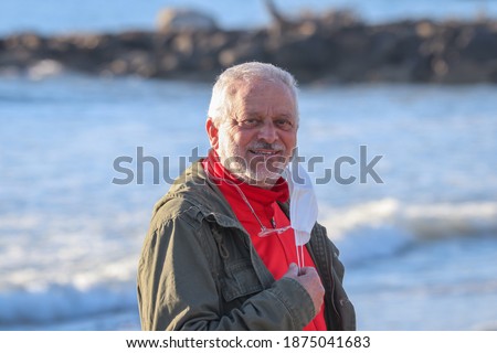 Portrait of smiling mature man taking off his surgical mask, on marine background.