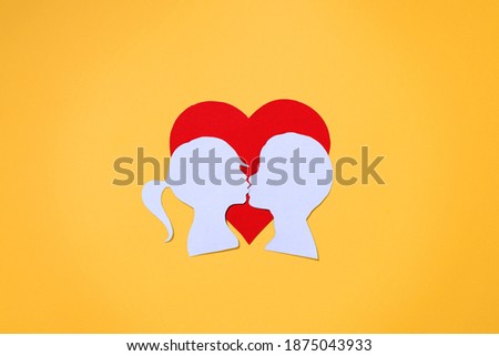 Red heart and couple girl and boy kissing, paper cut silhouettes. Flat lay, yellow background. Concept Valentine's Day, wedding, first love