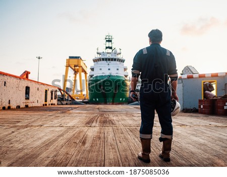 Marine Deck Officer or Chief mate on deck of offshore vessel or ship , wearing PPE personal protective equipment - helmet, coverall. Ship is on background Royalty-Free Stock Photo #1875085036