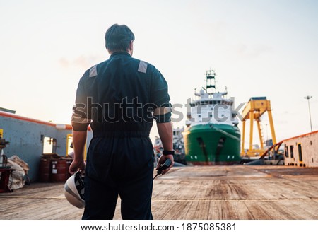 Marine Deck Officer or Chief mate on deck of offshore vessel or ship , wearing PPE personal protective equipment - helmet, coverall. Ship is on background Royalty-Free Stock Photo #1875085381