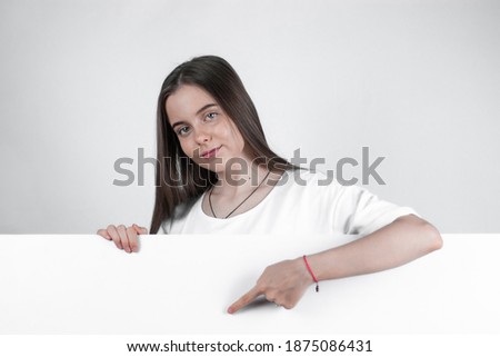 A teenage girl is holding a white blank sheet of paper and smiling while showing an empty board.