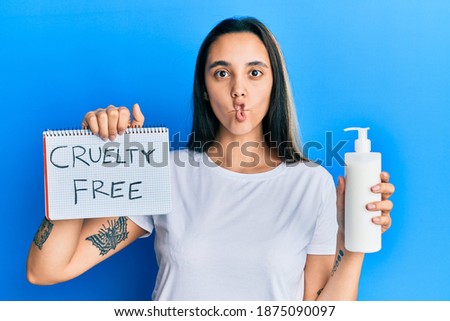 Young hispanic woman holding cruelty free cosmetics making fish face with mouth and squinting eyes, crazy and comical. 
