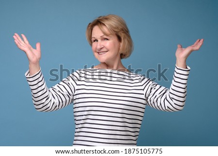 Old happy woman raising hands up, celebrating winning. Isolated over blue background