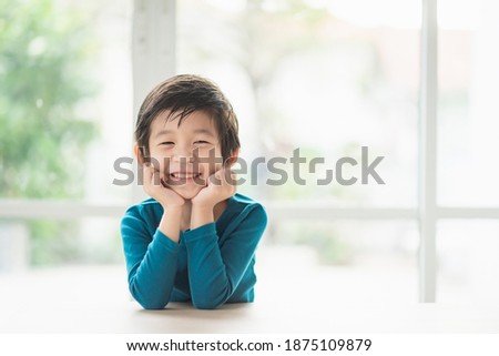 Cute Asian child resting chins on hands on wood table with copy space on right Royalty-Free Stock Photo #1875109879