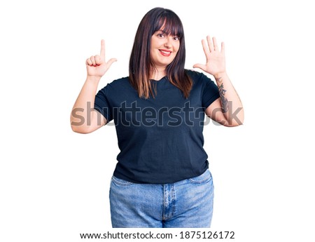 Young plus size woman wearing casual clothes showing and pointing up with fingers number seven while smiling confident and happy. 