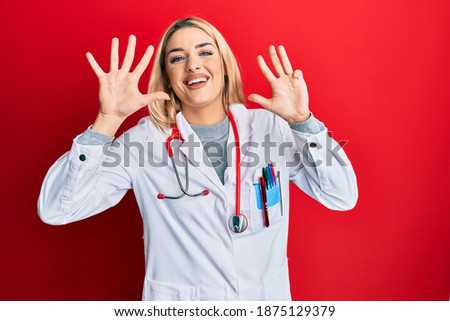 Young caucasian woman wearing doctor uniform and stethoscope showing and pointing up with fingers number nine while smiling confident and happy. 