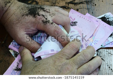 Man's hands, soiled with mud, covered the hryvnia scattered on the table.. High quality photo