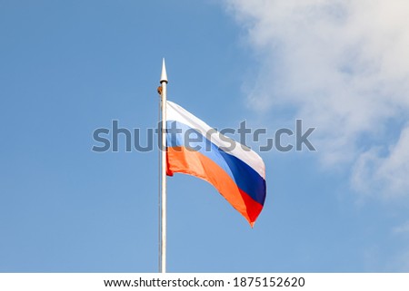 The flag of the Russian Federation flutters in the wind against the blue sky
