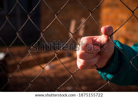 Close-up of a woman in a jacket holding her hands behind a mesh fence
