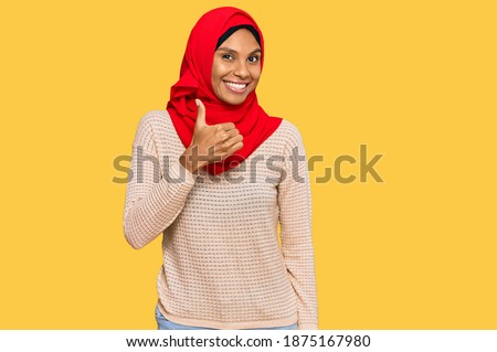 Young african american woman wearing traditional islamic hijab scarf doing happy thumbs up gesture with hand. approving expression looking at the camera showing success. 