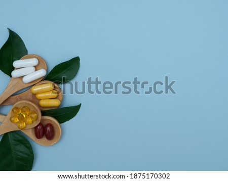Flat lay of vitamins, minerals, pills in wooden spoons and green leaves on a light blue background with copy space, top view. Integrative medicine. Medicines to improve immunity Royalty-Free Stock Photo #1875170302