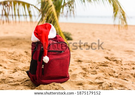 Santa Claus hat on backpack standing on sand beach. Christmas and New Year celebration. Nobody.