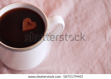 White cup of coffee with heart shaped sugar on pink textile background. Concept of love. Copy space