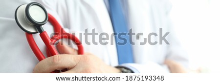 Close-up of qualified clinic medical worker holding clipboard and red stethoscope. Doctor working in luxury hospital. Modern medicine and patient appointment concept