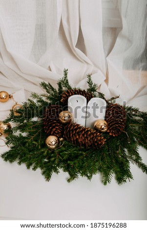 Scandinavian christmas card with white fabric and christmas wreath with white candles inside. Green fir branches, pine cones, golden balls and candles on white background with space for text.